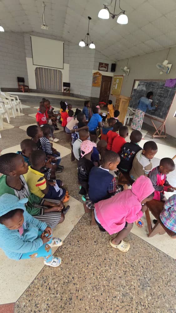 Children seated together on benches inside the church at 5 Day Club
