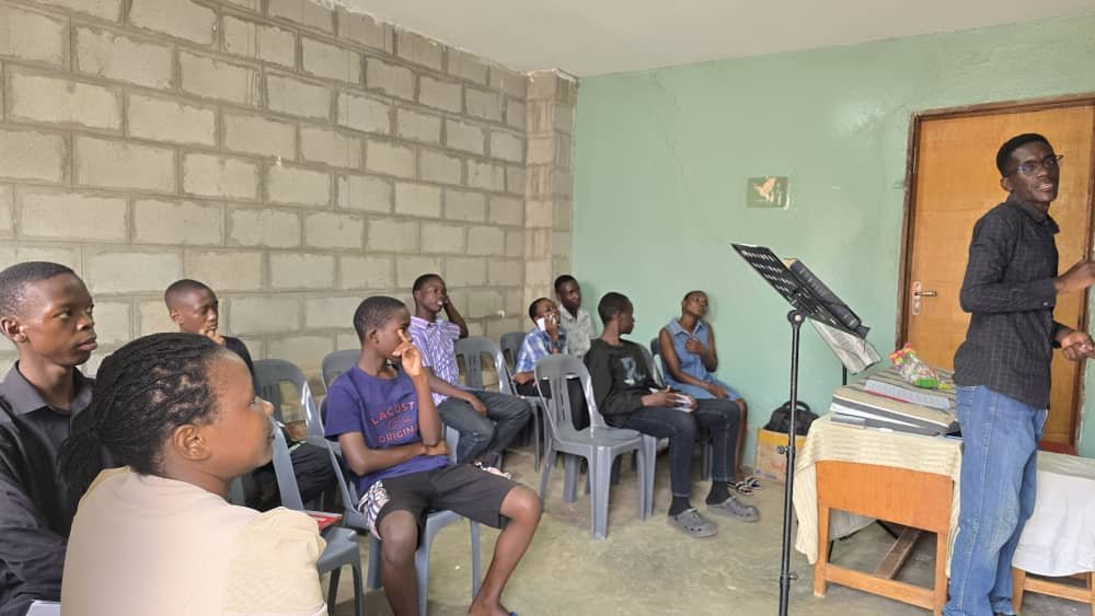 Young people seated around a leader teaching beside a chalkboard at 5 Day Club