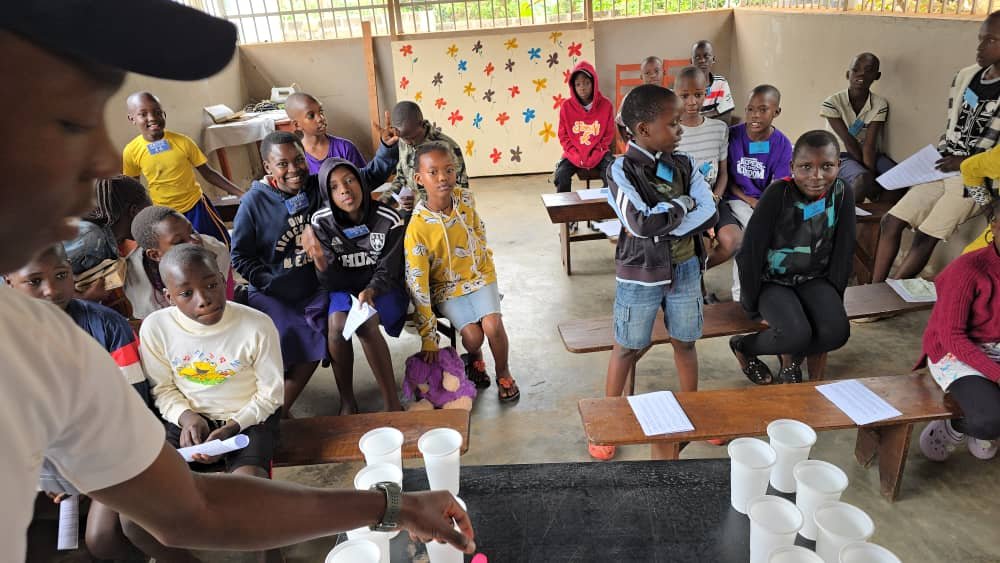 Children and leaders gathered beside a table with paper cups at 5 Day Club