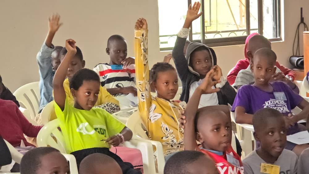 Children raising their hands during a gathering at 5 Day Club